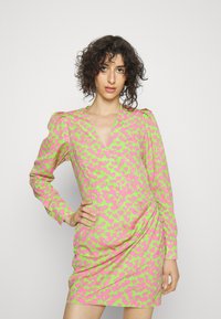 Vestido de mangas compridas em verde brilhante com padrões de corações cor-de-rosa, apresentando um decote em V e franzido na lateral para adicionar textura.