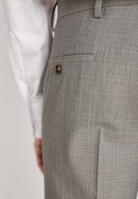 Pantaloni a quadri grigi con una singola tasca posteriore e dettaglio con bottone, caratterizzati da una vestibilità slim e una texture di tessuto fine.