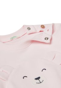 Světle růžová mikina s kulatým výstřihem, s patentkami a designem medvídka na přední straně. Vyrobena z měkké tkaniny s žebrovanou strukturou.