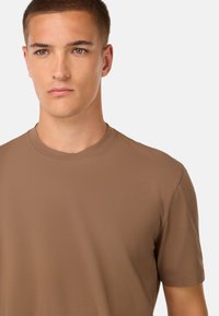 Hnědé krátké rukávy bavlněného trička s kulatým výstřihem. Hladká textura, přiléhavý tvar a minimální detaily šití.