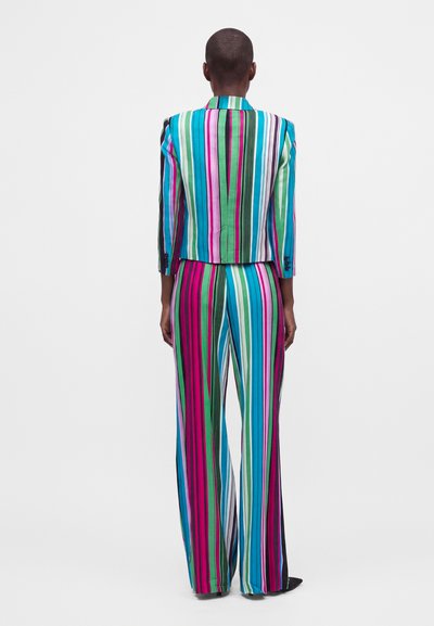 Personne vue de dos portant un costume éclatant avec des rayures verticales vertes, roses, bleues et blanches sur la veste et le pantalon à jambes larges.