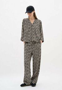 Button-up top and wide-leg pants in a black and beige abstract pattern. The fabric appears soft with a relaxed fit. Paired with a black cap.