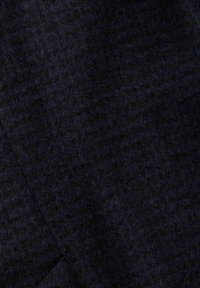 Tmavá vlněná látka s texturovaným povrchem, vykazující hlubokou černou barvu s jemnými variacemi. Vyznačuje se mírně chlupatým vzhledem.
