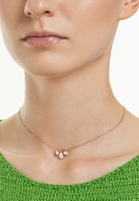 Nærbillede af en persons hals iført et delikat halskæde i rosaguld med tre små diamantpendanter, iført en tekstureret grøn top.