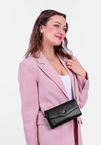 Schwarze Leder-Umhängetasche mit Kettenriemen und Umschlagdesign, mit einem silbernen Logoakzent auf der Vorderseite.