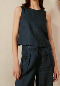 Top senza maniche blu navy in tessuto strutturato, abbinato a pantaloni a vita alta con dettagli a bottone e pince. Design semplice e moderno.