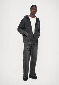 Σκοτεινό γκρι ζακέτα με φερμουάρ και υφή, συνδυασμένη με φαρδιά γκρι τζιν παντελόνια που διαθέτουν λεπτό μοτίβο και προσαρτημένη λεπτομέρεια τσέπης.