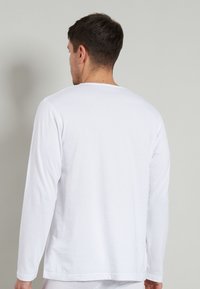 Long-sleeve white cotton t-shirt with a relaxed fit, round neckline, and smooth texture, viewed from the back.