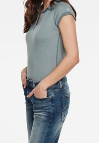 Polo de color azul claro con mangas cortas y cuello, combinado con unos jeans de mezclilla azul oscuro. Presenta un diseño sencillo y un corte ajustado.