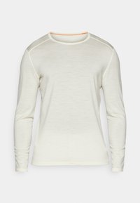 Chemise à manches longues de couleur crème, avec un col rond et des coutures orange, au toucher lisse. Design simple sans motifs supplémentaires.