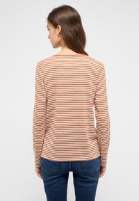 Langärmliges Shirt mit orange-weißen horizontalen Streifen, Rundhalsausschnitt, weichem Stoff und lockerer Passform, getragen mit blauen Jeans.