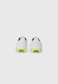 Scarpe da calcio bianche con tomaia sintetica liscia, accenti neri e tacchetti in un vivace verde neon, posizionate per una vista da dietro.