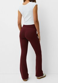 Pantalons évasés bordeaux avec une taille haute, fabriqués en tissu doux. Portés avec un crop top blanc ajusté et des chaussures plates.
