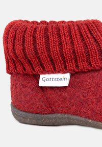 Røde uldslipper med en strikket kant, der har en struktureret overflade og en mørk gummisål. Inklusiv et synligt "Gottstein"-mærke.