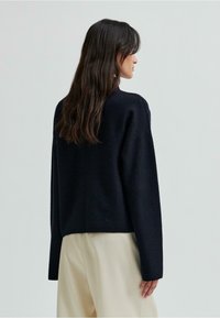 Granatowy, oversize sweter wykonany z miękkiej mieszanki wełny. Posiada obniżone ramiona, długie rękawy oraz luźny krój.