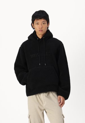 Zwarte fleece hoodie met een gestructureerde oppervlakte, kangoeroezak en capuchon met trekkoord. Voorzien van een reliëflogo op de voorkant, met een relaxte pasvorm.