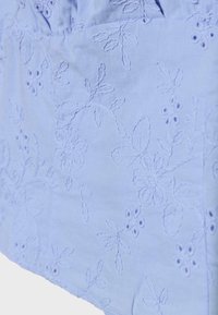 Tissu bleu clair avec motifs floraux et feuillages brodés, présentant de petits détails découpés sur toute la surface textile.