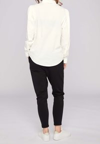 Biała koszula z długim rękawem, zaokrąglonym dołem i bufkami na ramionach, zestawiona z czarnymi zwężanymi spodniami i białymi trampkami.