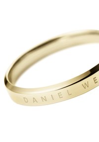 Zelta toņa metāla rokassprādze ar gludu apdari, kurai pa malām ir reljefā uzdruka "DANIEL WE". Moderns, minimālistisks dizains.