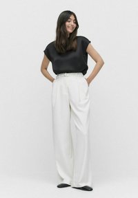 Sort satin kortærmet top med en afslappet pasform, parret med højtaljede, vide hvide bukser. Sorte spidse sko.