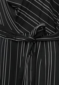 Robe en tissu noir avec des fines rayures blanches verticales, dotée d'un design portefeuille et d'une ceinture nouée à la taille. Texture lisse dans l'ensemble.