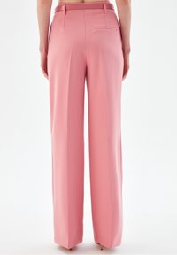 Wide-leg trousers in soft pink fabric. Features a smooth texture, tailored construction, single back pocket, and belt loops.