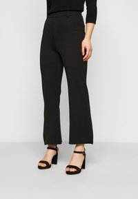 Svarta byxor med vida ben tillverkade av slät tyg, med en figurnära midja och ihopparade med kraftiga svarta klacksandaler.