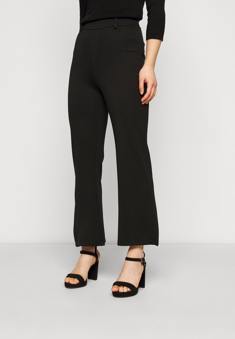 Svarta byxor med vida ben tillverkade av slät tyg, med en figurnära midja och ihopparade med kraftiga svarta klacksandaler.