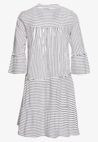 Páskované šaty v bílé a černé barvě, s tříčtvrtečními splývavými rukávy, vícevrstvou sukní a nařaseným detailem na zádech.