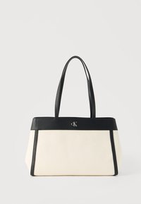 Κρεμ ορθογώνια τσάντα ώμου με μαύρο δερμάτινο περίγραμμα, διπλές λαβές και μικρό μεταλλικό λογότυπο «cK» στο κέντρο μπροστά.