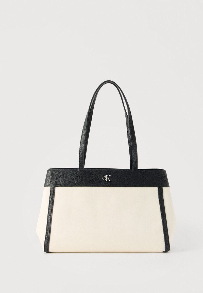 Κρεμ ορθογώνια τσάντα ώμου με μαύρο δερμάτινο περίγραμμα, διπλές λαβές και μικρό μεταλλικό λογότυπο «cK» στο κέντρο μπροστά.
