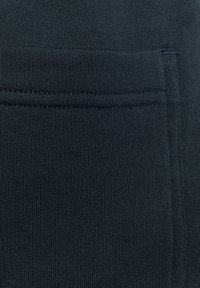 Mörkblått stretchy tyg med en slät yta. Har en sidficka med en sydd kant och fint ribbat detaljer.