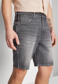 Shorts denim abu-abu dengan potongan lurus, dilengkapi dengan kantong depan, pencucian pudar, dan detail jahitan yang terlihat. Dihiasi dengan kancing metal.