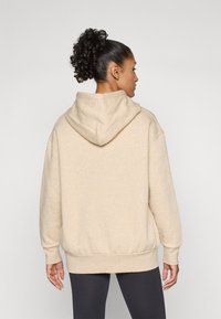Beige sweatshirt med huva, med ribbade manschetter och fåll, tillverkad av mjukt material, visad bakifrån.