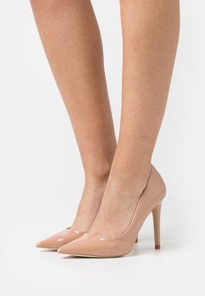 Béžové lodičky z lakované kůže s špičatou špičkou a štíhlým jehlovým podpatkem, s hladkým, lesklým povrchem.