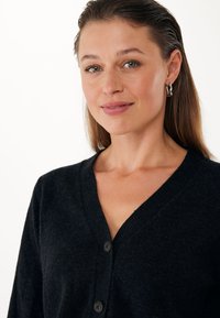 Cardigan nero con scollo a V, caratterizzato da tre bottoni, una texture morbida e maniche lunghe, su uno sfondo neutro.