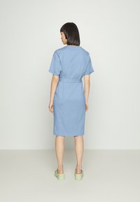 Vestido de algodão azul claro com mangas curtas, cintura ceifada, estilo até ao joelho e tamancos verdes planos. Design simples e aerodinâmico.