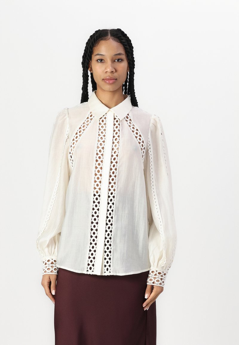 Weißes Blusenshirt mit Eyelet-Spitze entlang der Vorderseite und Ärmel, ausgestattet mit einem klassischen Kragen und gerafften Puffärmeln.