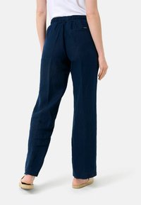 Osoba w granatowych luźnych spodniach z elastyczną talią i białych butach typu slip-on, stojąca tyłem do kamery.