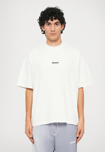 T-shirt bianco in cotone con scollatura rotonda e maniche corte. Presenta un piccolo logo testuale nero "BONSAI" sul petto. Texture liscia.
