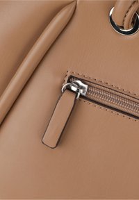 Klassinen vaalea keinonahkainen käsilaukku, jossa on vetoketjullinen tasku, sileä pinta, metalliset yksityiskohdat ja erottuvat tikkausyksityiskohdat.