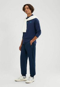 Marineblauw langemouwen top met een kraag, met een lichtblauw zakdetail; gecombineerd met bijpassende taps toelopende broek en witte sneakers. Gladde textuur.