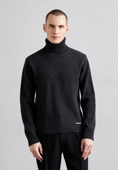 Pull à col roulé gris foncé en tissu doux avec des bords côtelés aux poignets et à l'ourlet, doté d'un petit logo près du bas. Texture lisse.