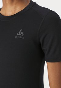 T-shirt noir Odlo à manches courtes avec col rond. Il présente un tissu lisse, des coutures contrastantes et un logo gris subtil sur la poitrine.
