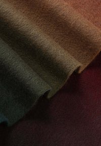 Des rouleaux de tissu feutré dans des teintes vertes, brunes et bordeaux, présentant une texture douce et une surface uniforme avec un aspect légèrement duveteux.