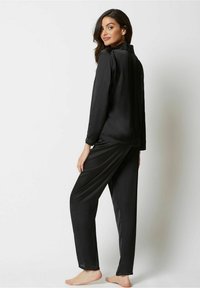 Zwart satijnen pyjama-set met een lange mouw top met een nepkraag en bijpassende broeken met een losse pasvorm. Glad textiel overal.