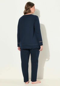 Navyblaues Loungewear-Set bestehend aus einem langärmeligen Oberteil mit gewelltem Saum und Detail, kombiniert mit passenden geraden Hosen. Weiches Material.