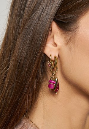 Gouden ringoorbellen met roze steen en gouden bedel die aan de linkeroor van een persoon worden gedragen, met zichtbaar bruin haar.