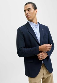 Blazer azul marino texturizado con solapas de muesca, un bolsillo y dos botones; combinado con una camisa a rayas azul claro y pantalones caqui.