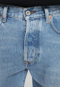 Ljusblå denimjeans med en märkbar blekningseffekt, med kopparaccenter, synlig sömnad och vanliga framfickor.